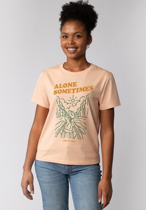 Perzikkleurig katoen T-shirt met een groen grafisch ontwerp met de tekst "ALONE SOMETIMES" en een zon boven een figuur in een landschap. Korte mouwen.