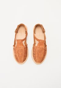 Brune lærsandaler med vævet overdel, åben tå-design, ankelslynge med spænde og en flad sål med tekstureret finish.