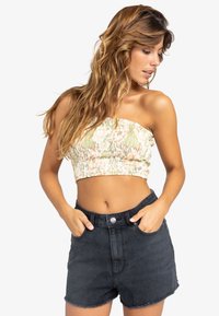 Stropeløs cropped top i et lyst blomsterprint med grønne og pink nuancer, stylet med højtaljede sorte denim shorts med en frynsedetalje.