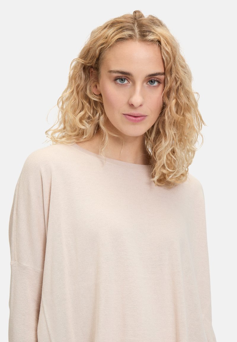 Pull oversized beige clair en tissu doux et texturé. Il présente un large col rond et des épaules tombantes.