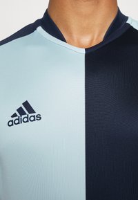 Jersey deportivo de Adidas, con un diseño dividido que presenta azul claro en un lado y azul marino oscuro en el otro. La tela tiene una textura suave, con el logo en el pecho.
