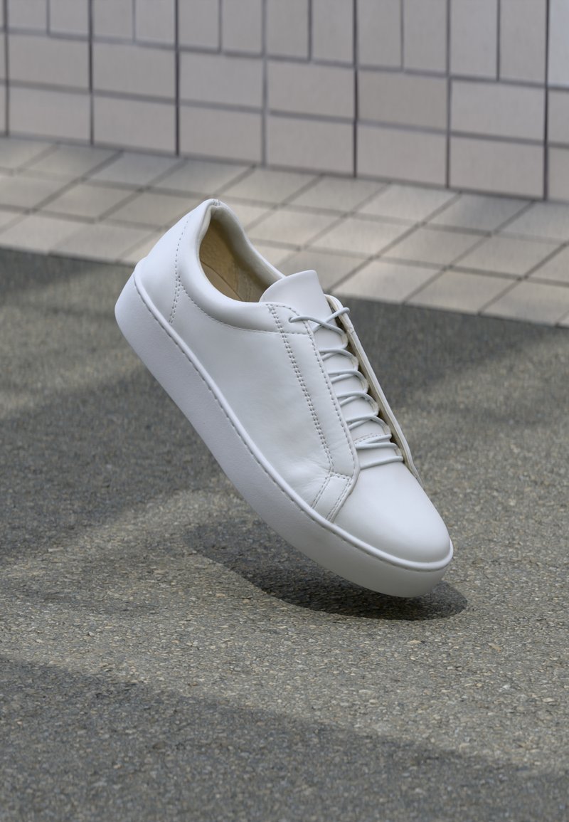Zapatilla blanca de piel con puntera redonda, suela plana y seis pares de ojetes. Textura suave y diseño minimalista con detalles de costura.