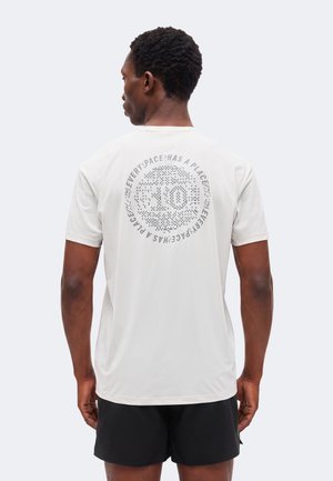 Hombre con camiseta blanca con diseño circular pixelado y texto "Every pace has a place" alrededor del número 10 en la espalda, combinado con pantalones cortos negros.