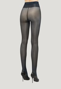 Collant neri trasparenti con finitura opaca, vita alta e punte rinforzate. Indossati con décolleté nere con tacco a spillo, che evidenziano una vestibilità uniforme.