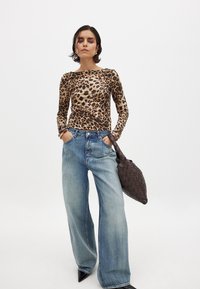 Leopardi prindiga pikkade varrukatega topp, kitsas disain. Lahtised heledat pesu denimist teksad, laiad sääred. Must tekstuuriga käekott, millel on kudumismuster.