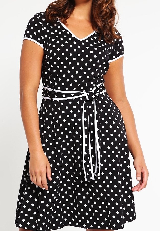 Svart klänning med vita prickar, korta ärmar, V-ringning, åtsittande midja med bälte, utställd kjol, lättviktsmaterial.