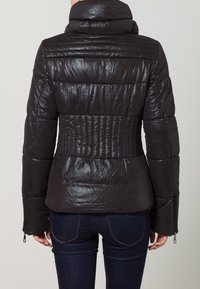 Giacca nera imbottita con finitura lucida, collo alto e vita aderente. Presenta una texture a coste e polsini con zip.