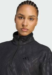 Pull en polaire noir avec col zippé mi-haut, présentant un motif texturé subtil et un logo brodé sur la poitrine gauche.