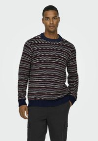 Pull en maille navy avec un motif blanc et bordeaux, manches et col côtelés. Le tissu a une apparence texturée et confortable.