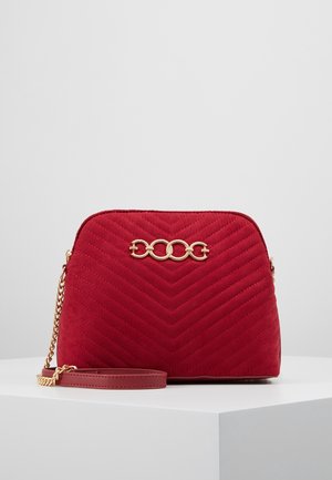 Czerwona pikowana torebka na ramię z łańcuszkowym paskiem, złotymi elementami oraz zygzakowatym wzorem przeszyć na gładkiej tkaninie.