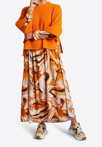 Pull orange côtelé superposé à une robe marbrée orange et blanche, accompagné de baskets multicolores.