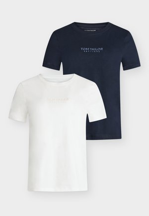 Femme portant un t-shirt blanc et un pantalon large rayé bleu clair, tenant un sac à main rouge et portant des ballerines rouges.