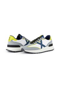 Baskets en gris, blanc et marine avec des accents jaunes fluo. Matériaux en daim texturé et en mesh. Semelle en caoutchouc épaisse avec un motif de bande noire.