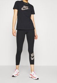 Svart t-shirt med ett leopardmönstrat Nike-logotyp, i kombination med svarta leggings som har en matchande logotyp på vaden, samt vita träningsskor.