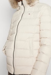 Tikkitakki vaaleanbeigenä, edessä vetoketju, tikattu muotoilu ja huppu, jossa tekoturkisreunus. Mukana sivutaskut ja resorireunaiset hihansuut.