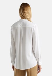 Bílá halenka s dlouhým rukávem a klasickým límcem, s plisé detaily na zadní straně a knoflíkovými manžetami. Hladká tkanina s volným střihem.