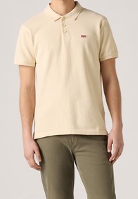 Polo crème en coton avec une texture douce, doté d'une patte de boutonnage à trois boutons et d'un petit logo rouge Levi's sur la poitrine.