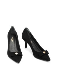 Black suede pointed-toe high heels with small bow and gold button detail, displayed side by side on a white background.