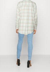 Camicia a maniche lunghe a quadri in verde chiaro e beige, realizzata in tessuto morbido, abbinata a jeans skinny blu chiaro e sandali neri con tacco alto.