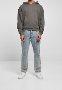 Sudadera gris de gran tamaño con un bolsillo frontal y cremallera corta; combinada con vaqueros descoloridos de un azul claro y zapatillas blancas.