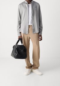 Lichtgrijze button-up shirt over een wit T-shirt, beige broek, witte sneakers en een zwarte leren tas met ronde handvatten.