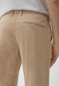 Beige katoenen broeken met een gladde textuur, voorzien van twee achterzakken met subtiele kleppen. Ontworpen met een rechte pasvorm en een middelhoge taille.