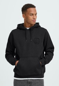 Juodas gobtuvinė sportinė palaidinė su priekiu kišeniu ir mėlynomis rankovėmis. Priekyje yra tekstūruotas logotipas, pagamintas iš minkštos, lygaus audinio.