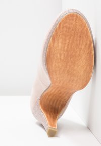 Chaussure à talon haut beige pour femme avec détail pailleté au talon et à la semelle, vue par le dessous sur fond blanc.