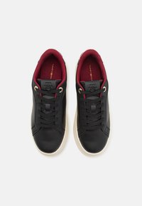 Svarta lädersneakers med en slät yta, rund tå, gyllene ögla och vinröd foder. Fäster Tommy Hilfiger-logotypen på tungan.