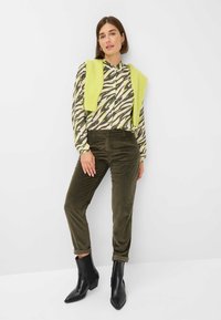 Bedruckte Bluse mit langen Ärmeln in Creme, Grün und Schwarz, kombiniert mit olivgrünen Cordhosen und schwarzen Stiefeletten mit spitzer Zehenpartie.