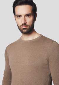 Brązowy dzianinowy sweter z długim rękawem, okrągłym dekoltem i dopasowanym krojem. Gładka tekstura i równomierne przeszycia na całej powierzchni.