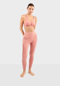 Roze sportset bestaande uit een aansluitende sportbeha met een mesh paneel en hoog-waist leggings met zijaccentdetails. Zachte stof textuur.