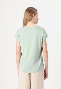 Top scurt de culoare verde deschis, cu guler rotund. Fabricat dintr-un material moale, are o croială lejeră și un tiv rotunjit.