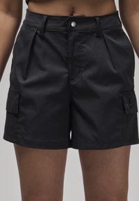 Pantaloni corti neri con vita aderente, fronte plissettato e tasche cargo sui lati. Realizzati in un tessuto liscio con dettagli di cucitura minimi.