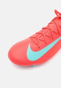 Röd fotbollssko med klarblå Nike-swoosh, snörning knuten och textilöverdrag av syntetmaterial mot vit bakgrund.