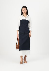 Costum format din două piese, cu dungi navy, având un top ajustat cu butoane și o cămașă albă cu guler. Completat cu o fustă dreaptă și sandale.