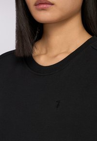 Svart sweatshirt med rund halsringning, ribbade ärmslut och en subtil logotyp på bröstet. Mjuk tygkvalitet med en slät yta.