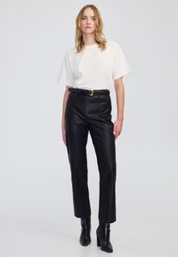 Czarne skórzane spodnie z prostym krojem, z przeszyciami z przodu i wysokim stanem. Połączone z luźną, białą koszulką z bawełny i czarnym paskiem.
