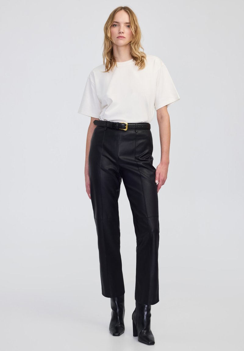 Czarne skórzane spodnie z prostym krojem, z przeszyciami z przodu i wysokim stanem. Połączone z luźną, białą koszulką z bawełny i czarnym paskiem.