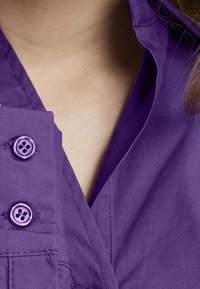 Lila Hemd mit Knöpfen, das einen Kragen, zwei Knöpfe und strukturierten Stoff aufweist. Beinhaltet Nähdetails an der Knopfleiste und den Kragenkanten.