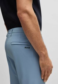 Light blue tailored pants with a smooth texture, featuring a concealed back pocket and subtle "BOSS" logo detail.