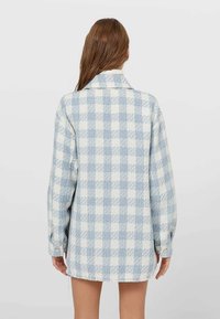 Modrá a bílá kostkovaná oversized košile s límcem, dlouhými rukávy a roztrhaným lemem; vyrobena z měkké, texturované látky.
