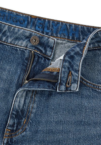 Jean en denim avec une teinte bleue, doté d'un zip, d'une fermeture à bouton en métal et de coutures contrastantes le long de la taille et des coutures.