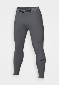 Leggings grises Nike Pro con una cinturilla a rayas negras, detalles de malla en los muslos y un pequeño logo negro en la parte inferior de la pierna.