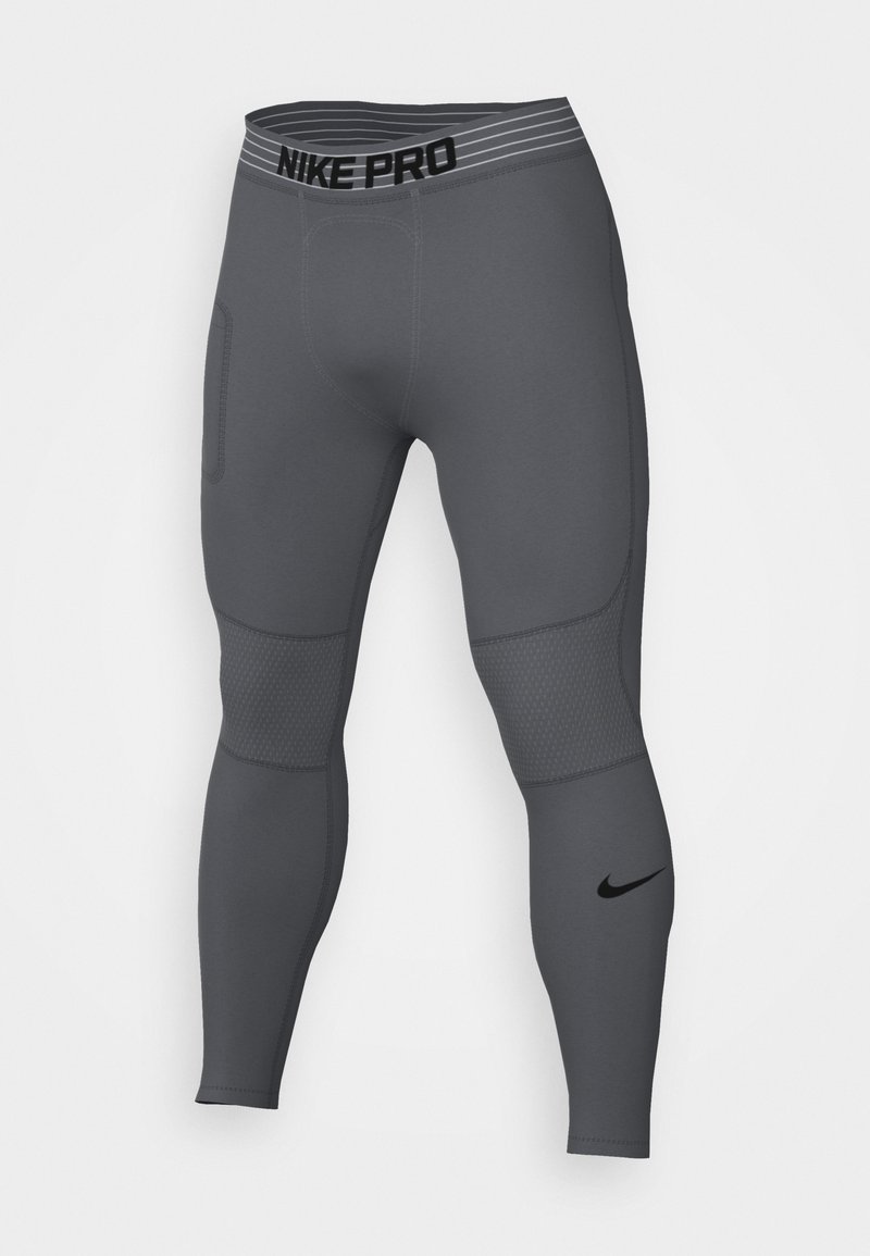 Leggings grises Nike Pro con una cinturilla a rayas negras, detalles de malla en los muslos y un pequeño logo negro en la parte inferior de la pierna.