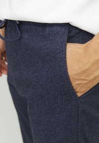 I pantaloni a spina di pesce blu navy presentano un tessuto testurizzato, una vita elastica con cordoncino e tasche laterali, mostrando un design sartoriale.