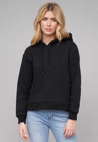 Black hoodie with a kangaroo pocket, drawstrings at the hood, ribbed cuffs, and hem. Fabric appears soft and textured, suitable for casual wear.