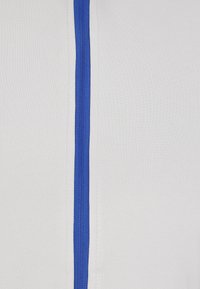 Tessuto bianco con un dettaglio di zip verticale blu. La superficie ha una texture liscia e una leggera elasticità.
