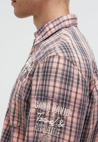 Kurzärmliges, kariertes Hemd in pinken, grauen und schwarzen Tönen. Verfügt über bestickte Texte und abgenähte Details, mit einem Kragen und Knopfverschlüssen.