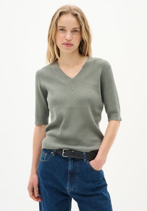 Maglione corto a maniche corte di un verde chiaro con scollatura a V e texture a coste, abbinato a jeans in denim blu a vita alta e una cintura nera.